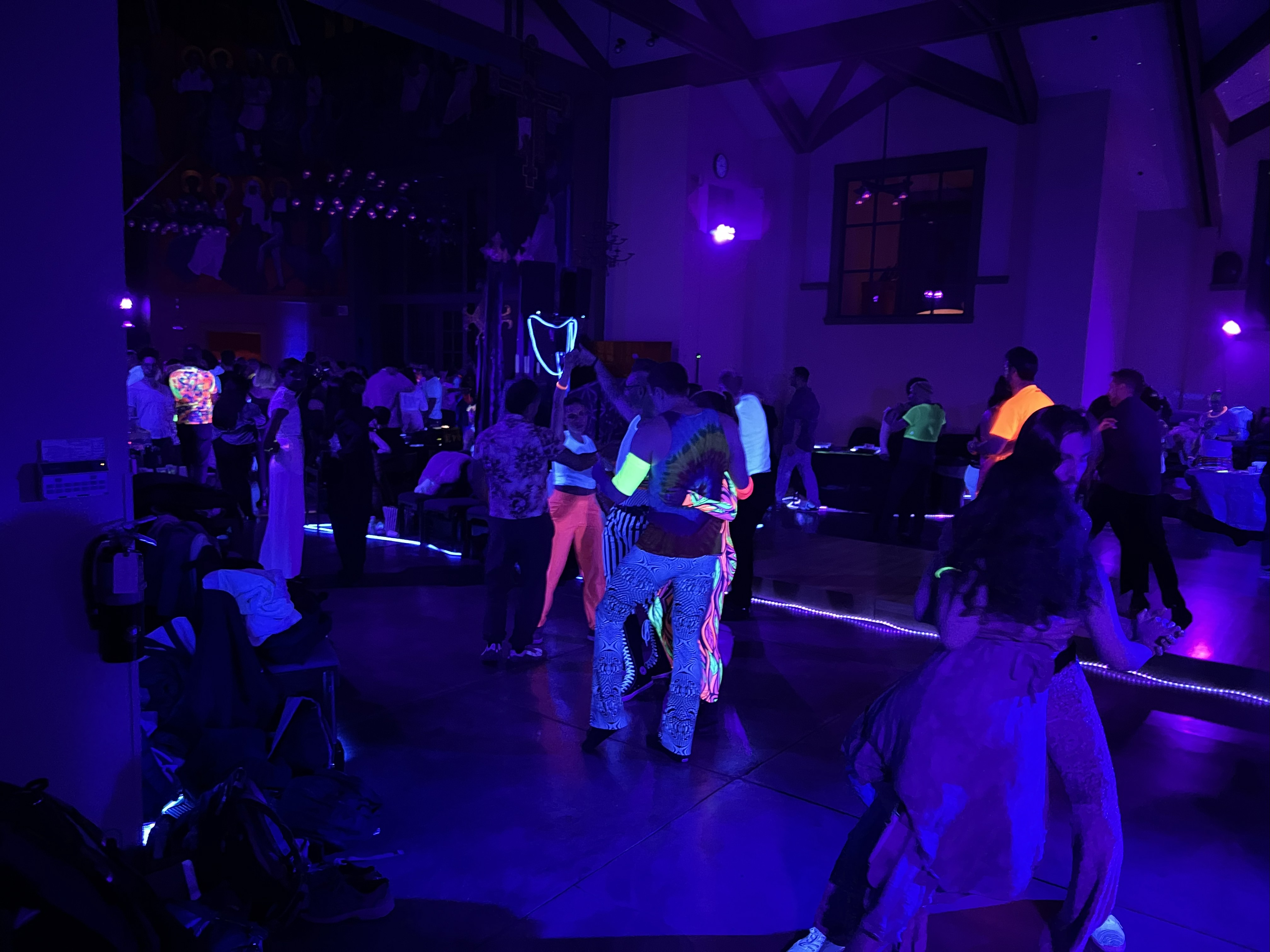 Dancers moving under black light during Mission Fusion in San Francisco, with neon outfits and glowing details.