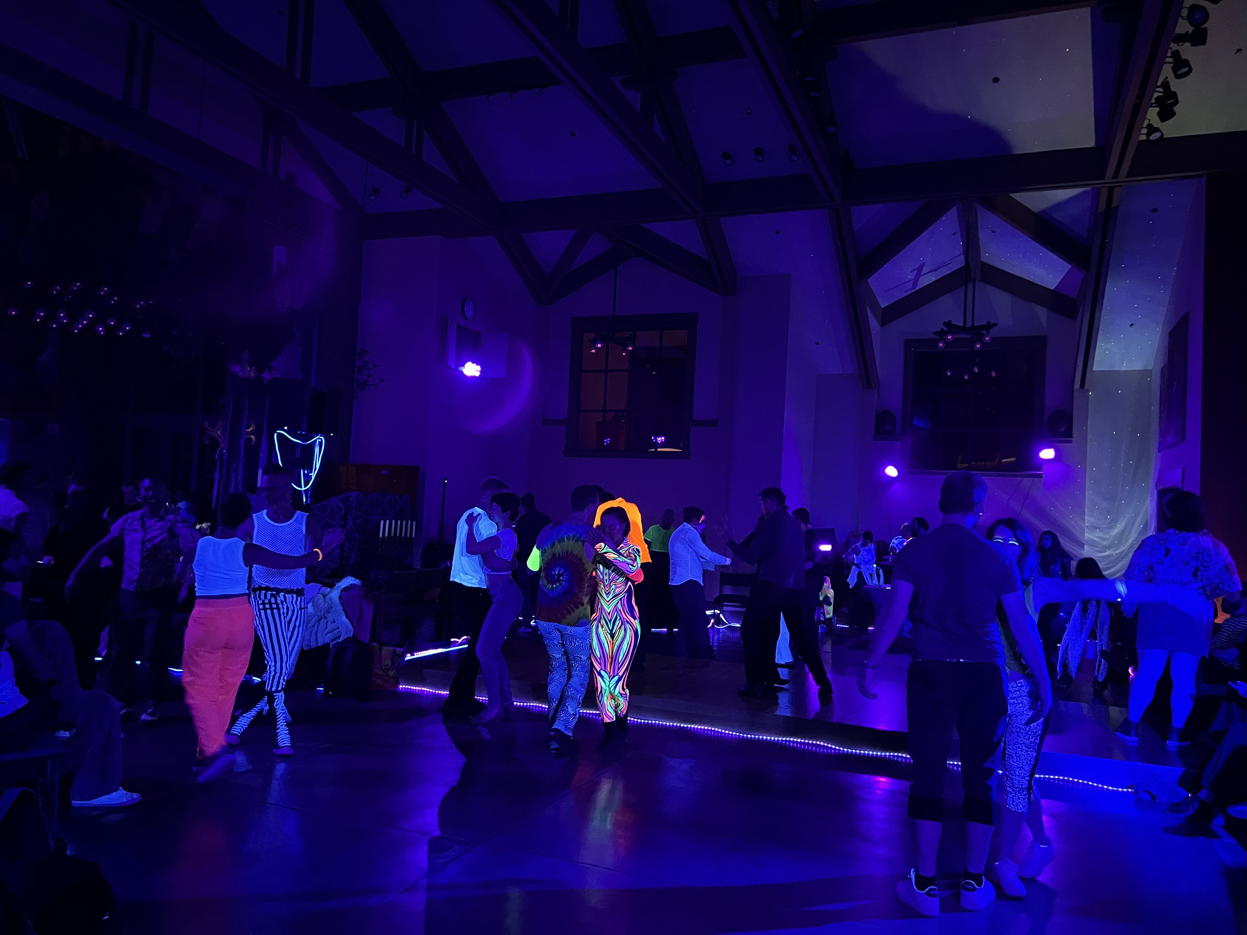 Crowded Mission Fusion Black Light Party dance floor glowing under neon lights at St. Gregory of Nyssa in San Francisco.