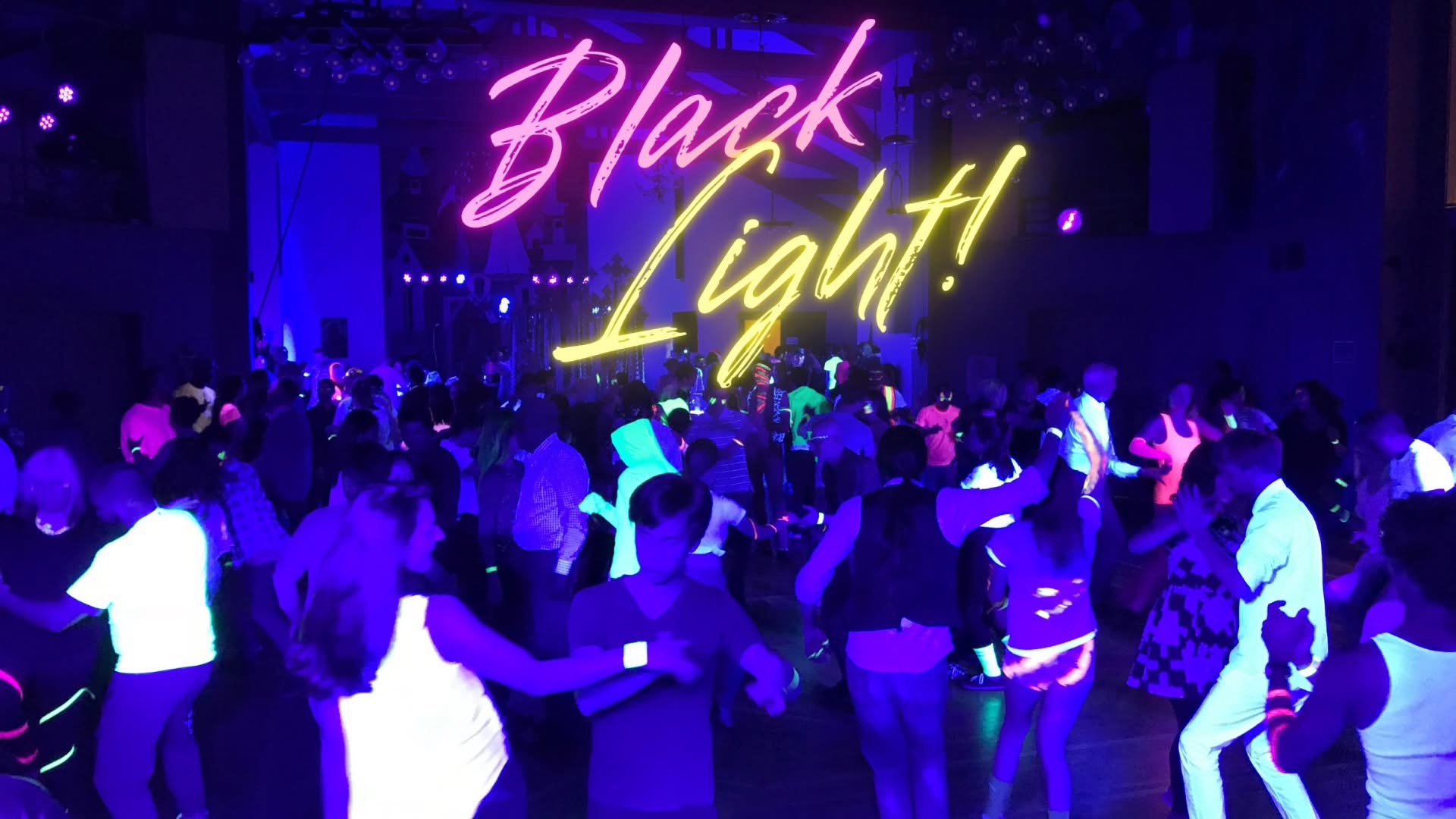 Wide view of Mission Fusion Black Light Party with the words Black Light glowing above the dance floor.