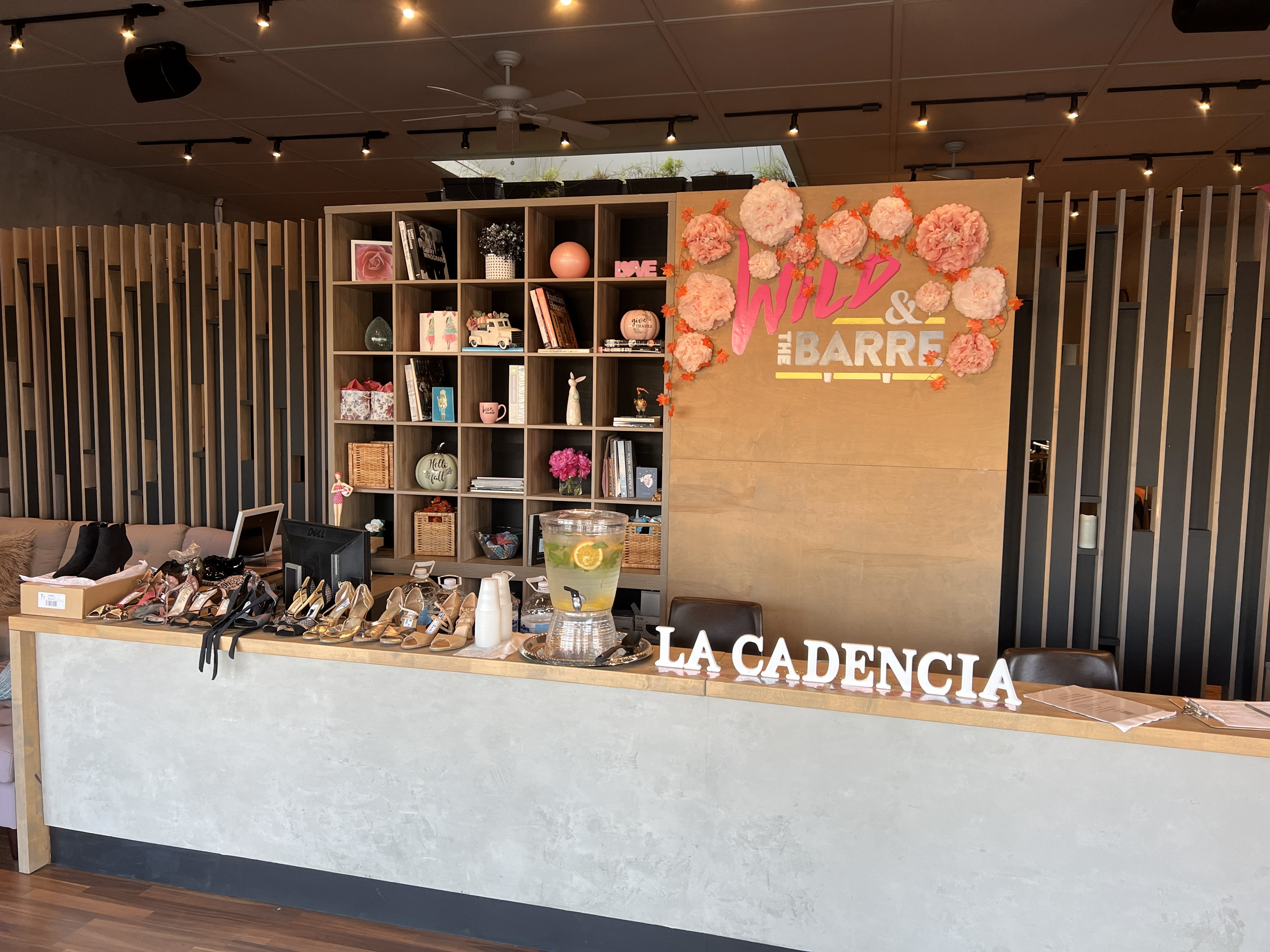 Front counter at Wild & the Barre with La Cadencia sign, flower decorations, and tango shoes for sale.