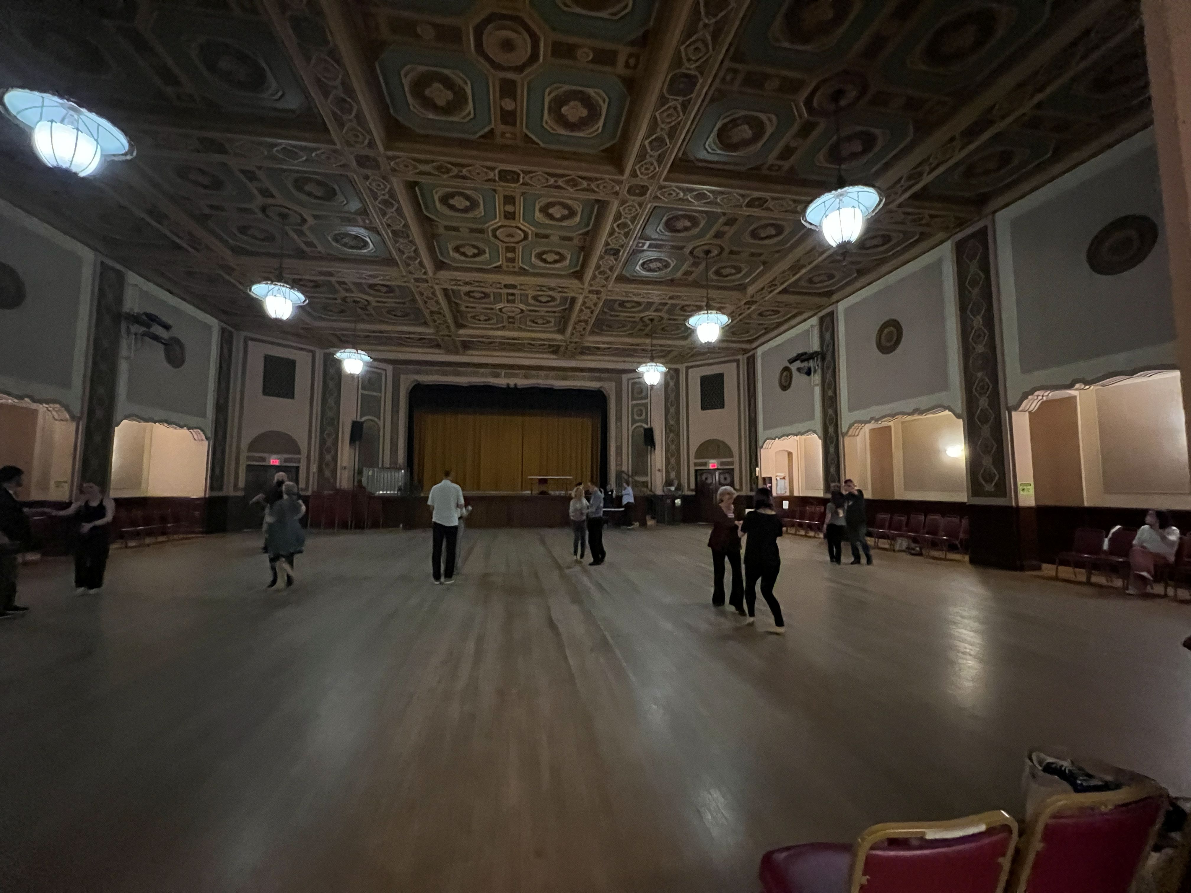 Wide view of the main dance hall with a spacious wooden floor and ornate ceiling at SwingOut House Party.