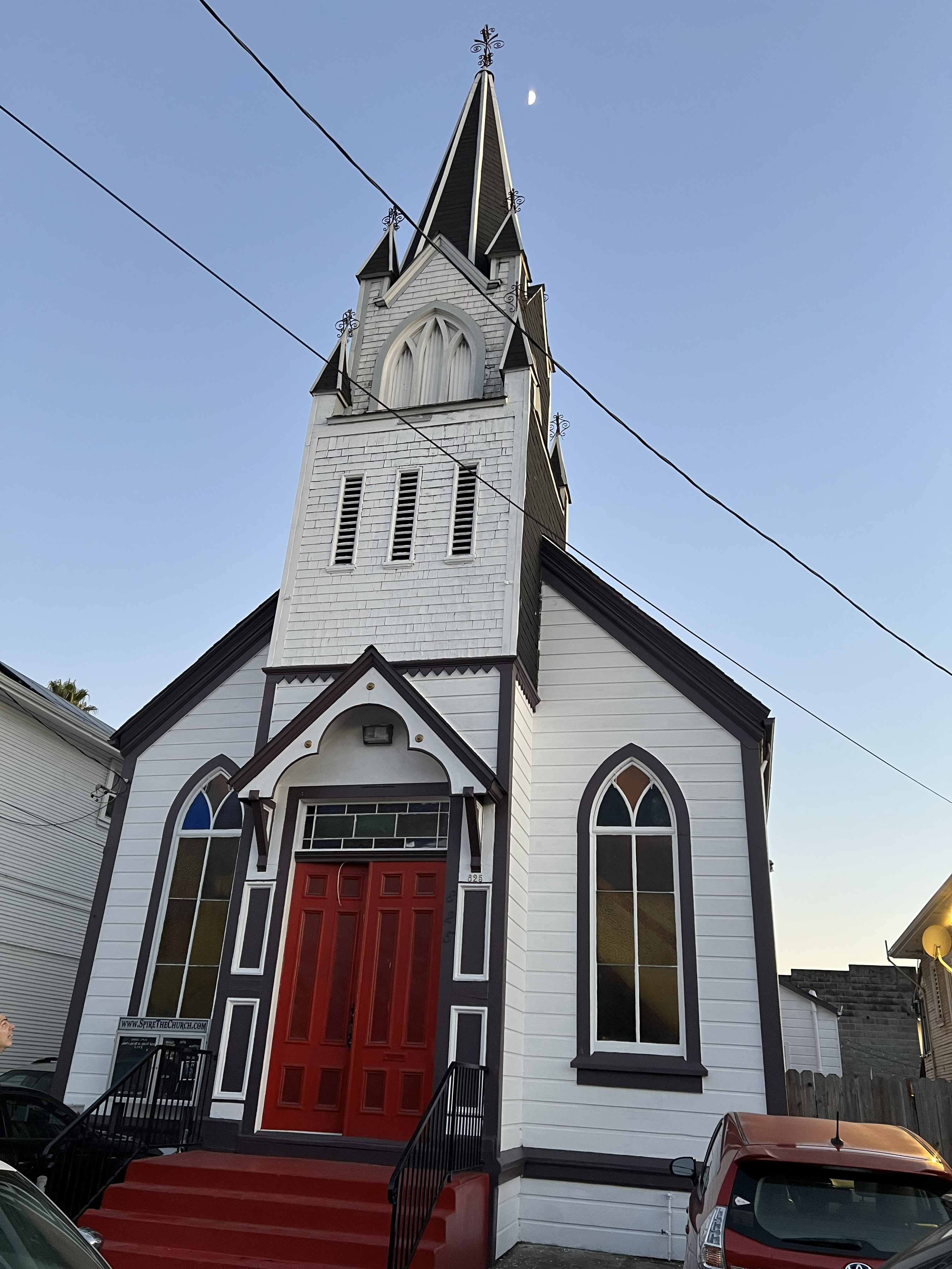 Exterior of Spire The Church in Oakland with red doors and tall spire at dusk.